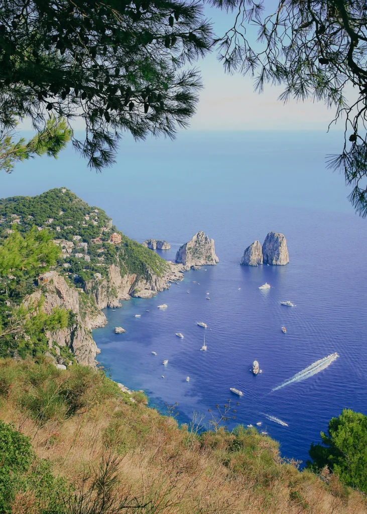 Capri's Faraglioni sea stacks seen from a high cliff path, boats in the blue water