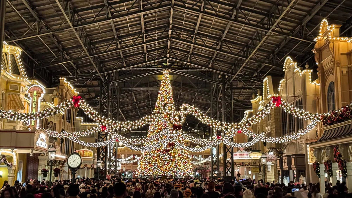 Tokyo Disneyland entrance at night with festive floral Mickey display and lit castle street