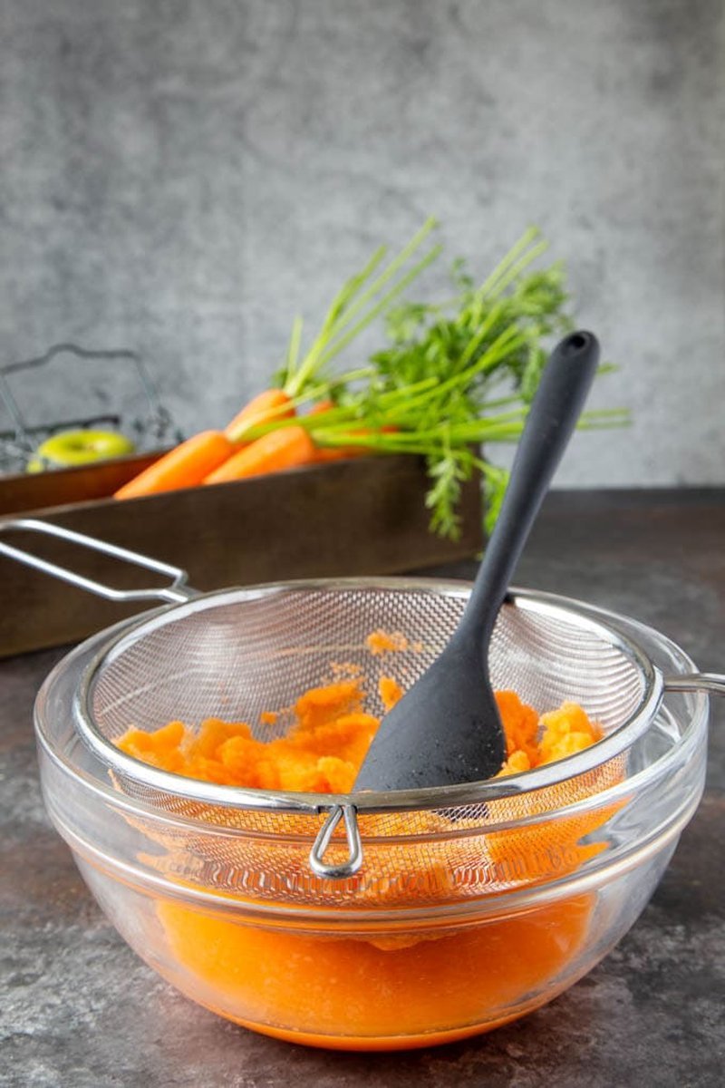Mashed carrots strained through fine mesh into glass bowl