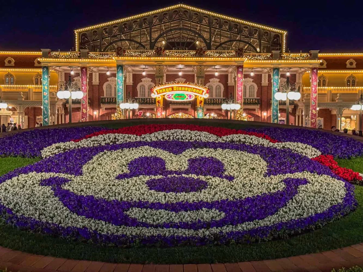 Tokyo Disneyland gate at night with festive floral garden and warm lights
