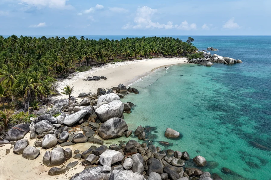 Aerial view of secluded crescent beach with palm forest in Bangka