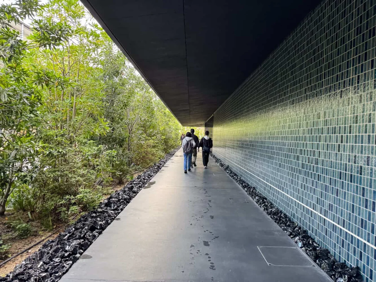 Glossy teal tiled wall beside a concrete path leading into teamLab Biovortex