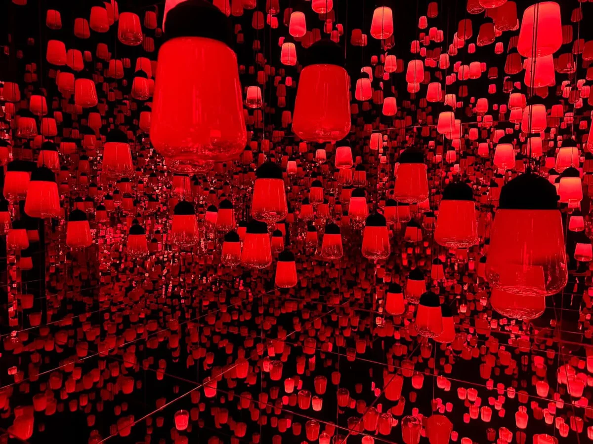 Hundreds of red glass lanterns reflected in a mirrored teamLab room
